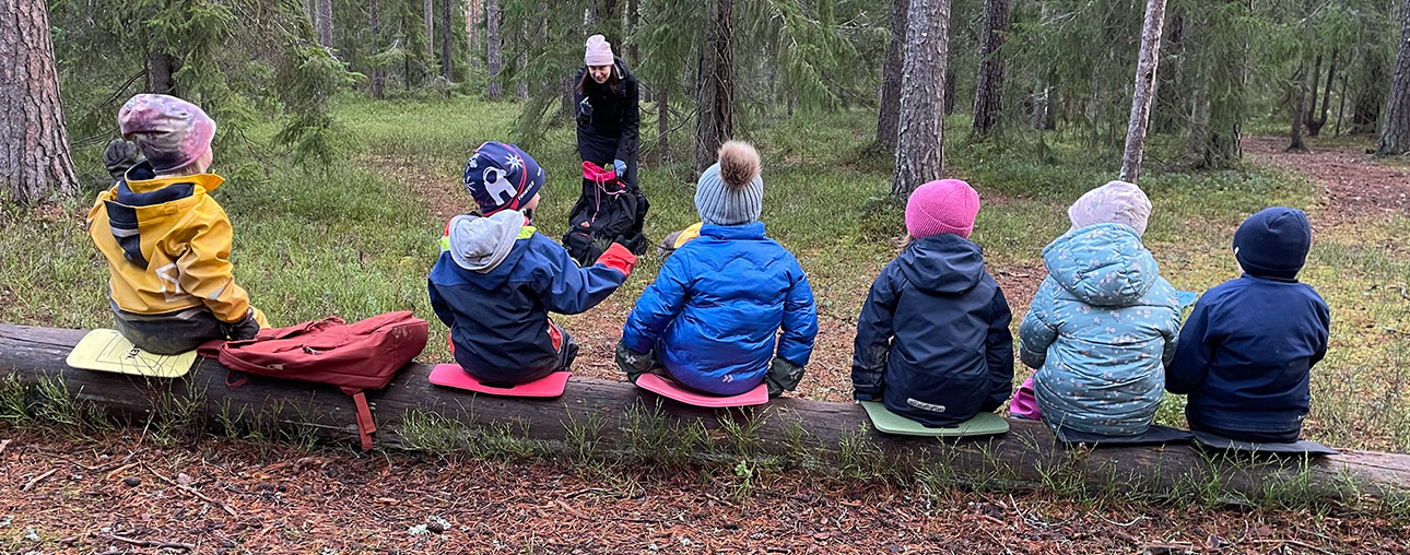 Foto på barn som sitter på en trädstock och tittar på Jenny och Azlan